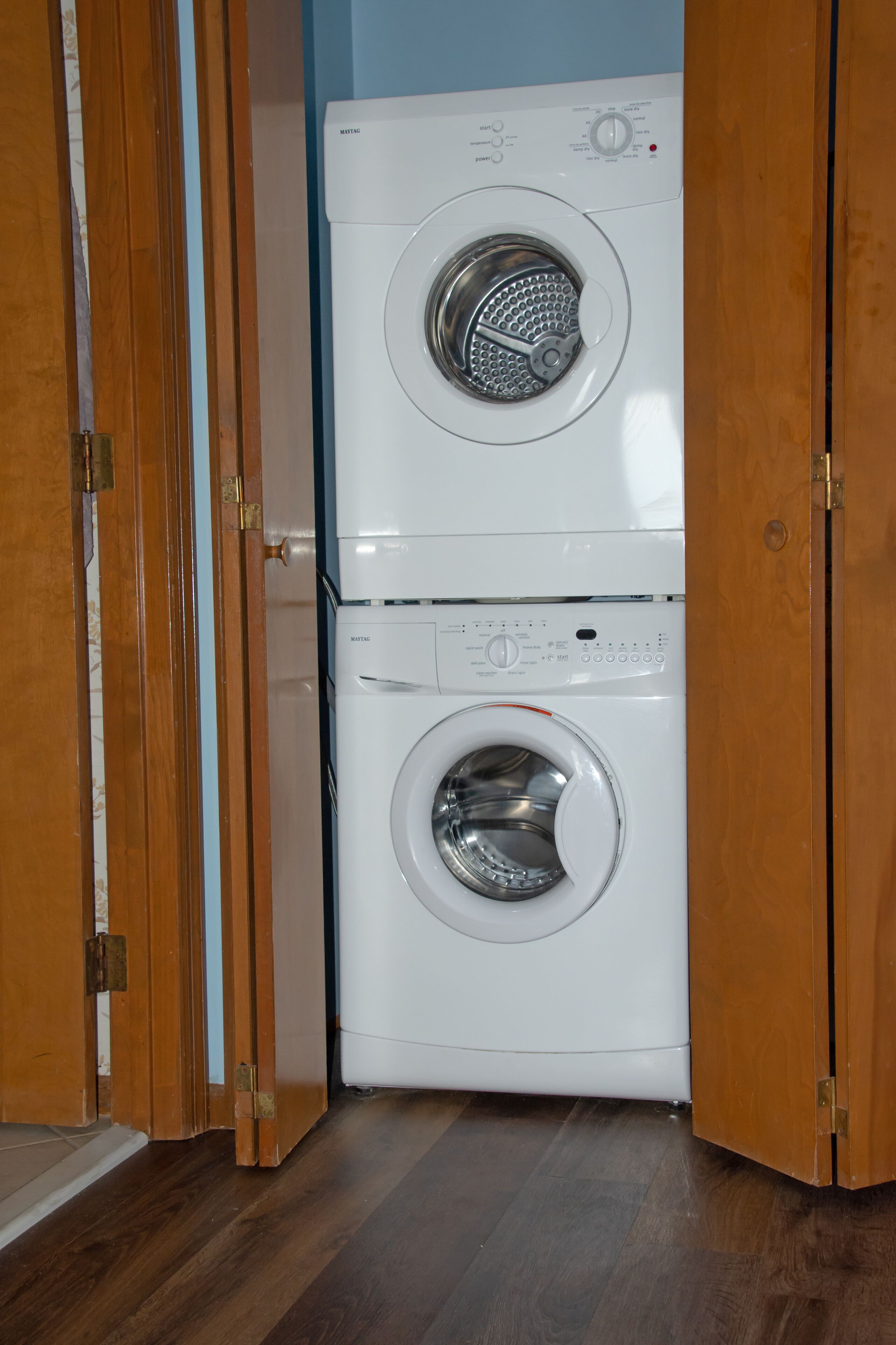 A front-loading washing machine in a laundry room with wooden doors.
