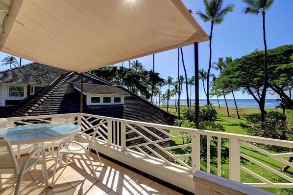 Un balcon avec une table et des chaises, donnant sur une zone côtière bordée de palmiers et offrant une vue sur l’océan.