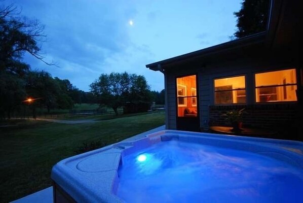 A hot tub in front of a house with a lit interior.