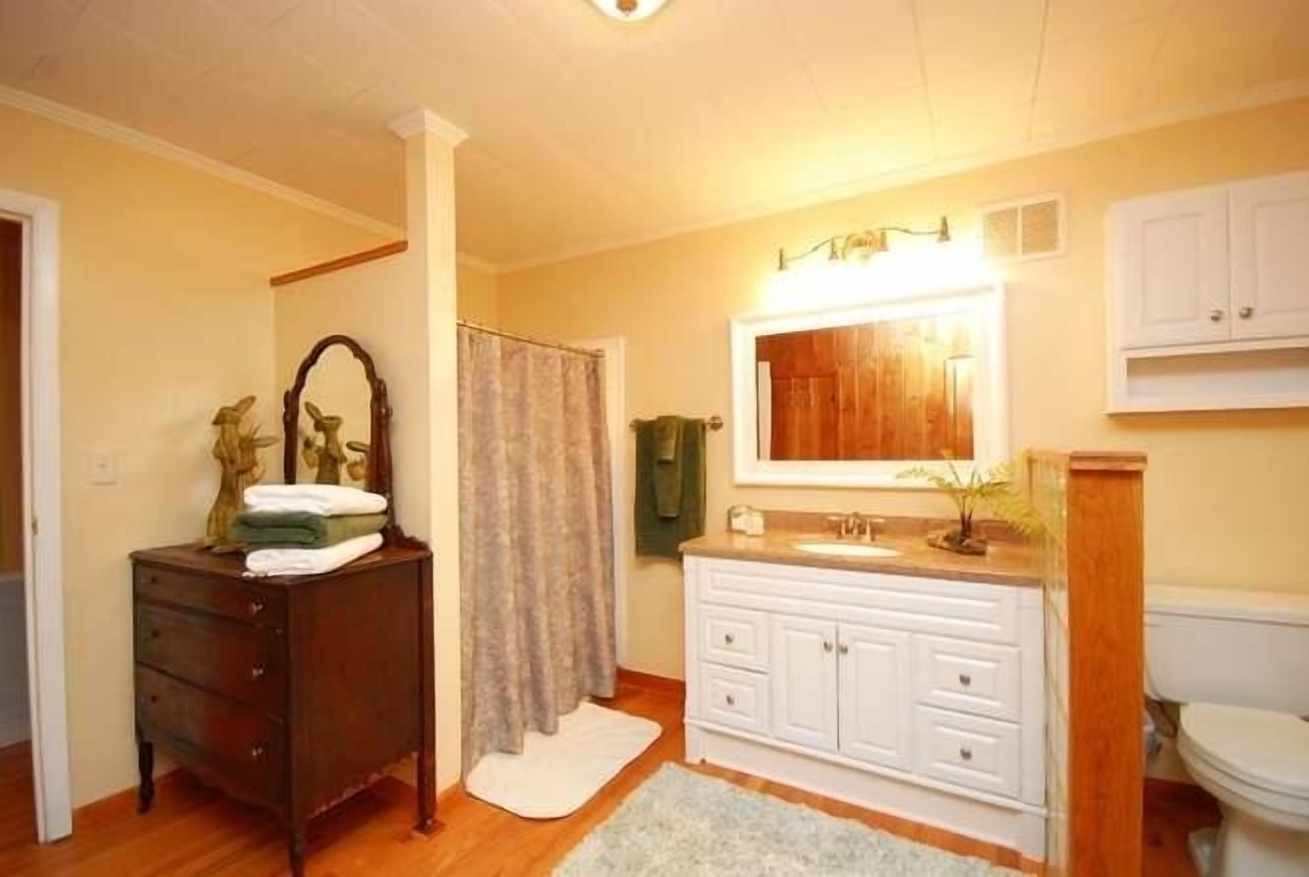 A bathroom with a wooden vanity, a mirror, a sink, and a toilet.