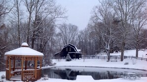 Schneebedeckte Landschaft mit einem hölzernen Pavillon, einem Bauernhaus und einem Teich.