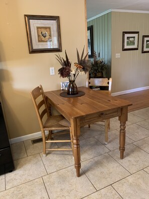 Un coin repas avec une table en bois, des chaises et un vase contenant des fleurs séchées.