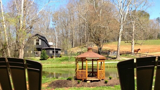 Zwei Adirondack-Stühle, die auf einen Teich mit einem Gazebo und einem Haus im Hintergrund zeigen.