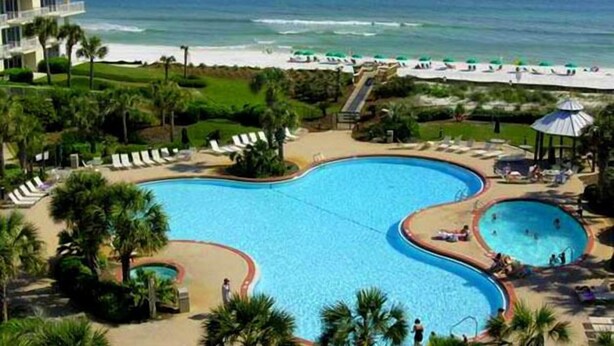 Ein Resort mit einem großen zentralen Pool, einem kleineren angrenzenden Pool und einem Strandbereich mit Sonnenschirmen.