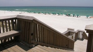 Eine Holzterrasse mit Blick auf einen Strand mit Sonnenschirmen und Menschen.