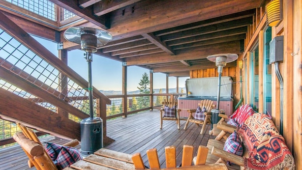 Eine Holzterrasse mit Sitzgelegenheit im Freien, einem Holzofen und Blick auf die Berge.