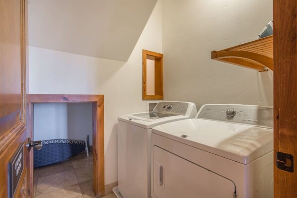 A laundry room with two washing machines, a wooden door, and a mirror on the wall.