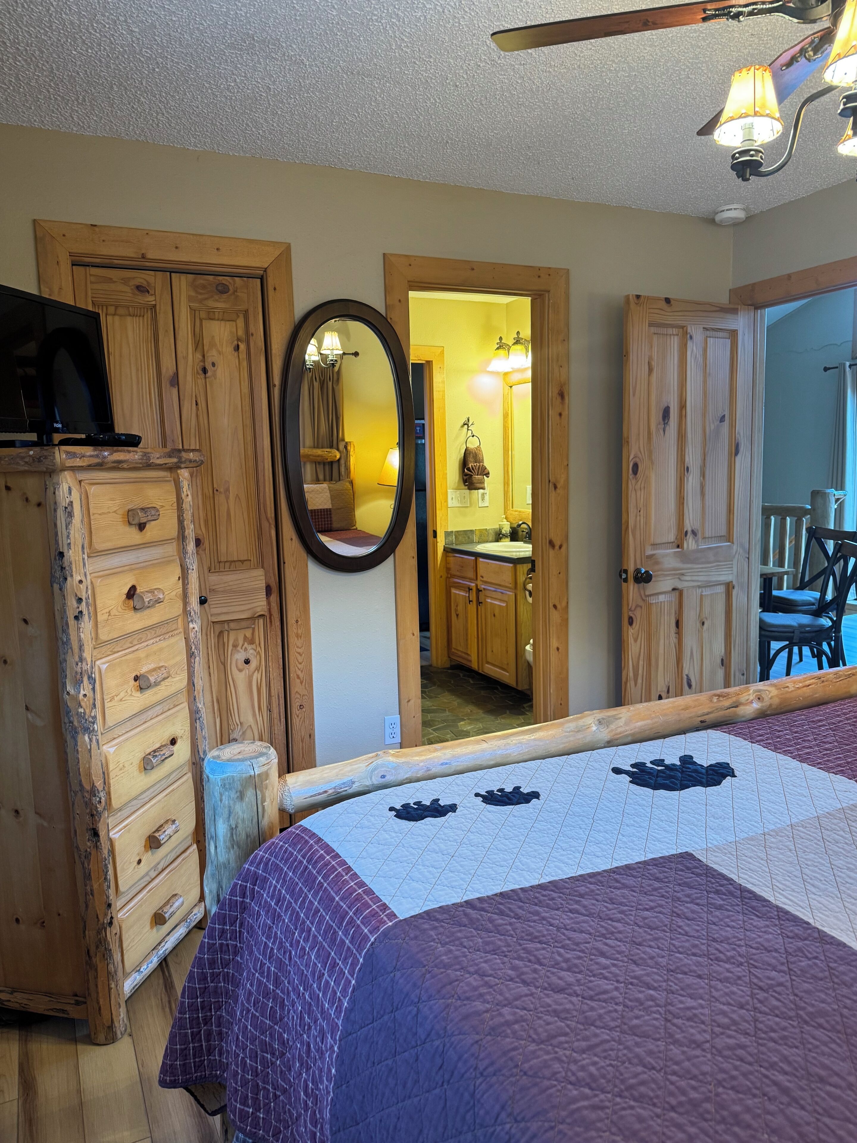 A room with a wooden dresser, a bed with a quilt, a mirror, and a ceiling fan.