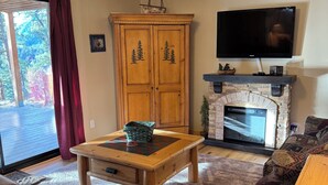 Una sala de estar acogedora con chimenea, televisor y un ventanal con cortinas.