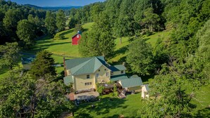 A large, single-story house with a green roof, surrounded by lush greenery and a small red barn. - Stunning Family/Friends Retreat,110 Private Acres, Renovated Historic Home (Madison)