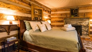 A wooden-framed bed with a quilted green bedspread and multiple pillows, a bedside table with a lamp, and a fireplace with a framed picture above it. - Stunning Family/Friends Retreat,110 Private Acres, Renovated Historic Home (Madison)