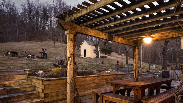 A wooden pergola with a table and benches, a small shed, and a hill with a house in the background. - Stunning Family/Friends Retreat,110 Private Acres, Renovated Historic Home (Madison)