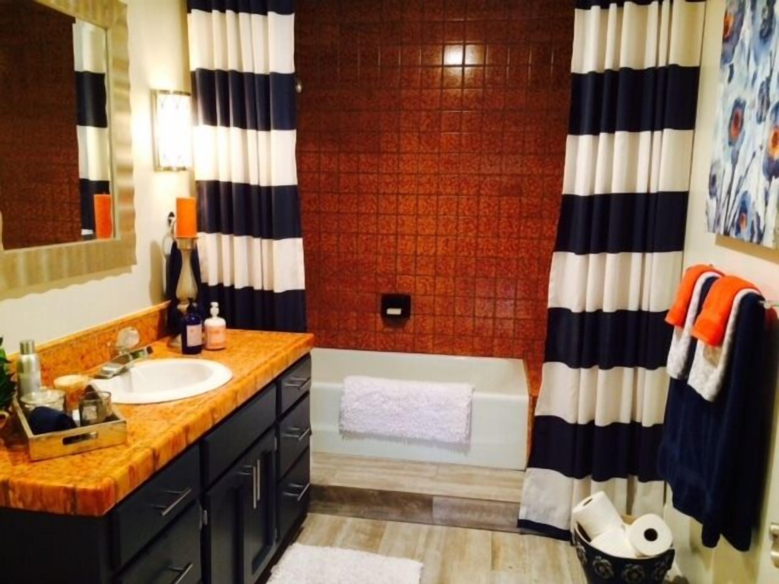 Un baño con tocador de madera, lavamanos blanco, bañera y cortinas a rayas.