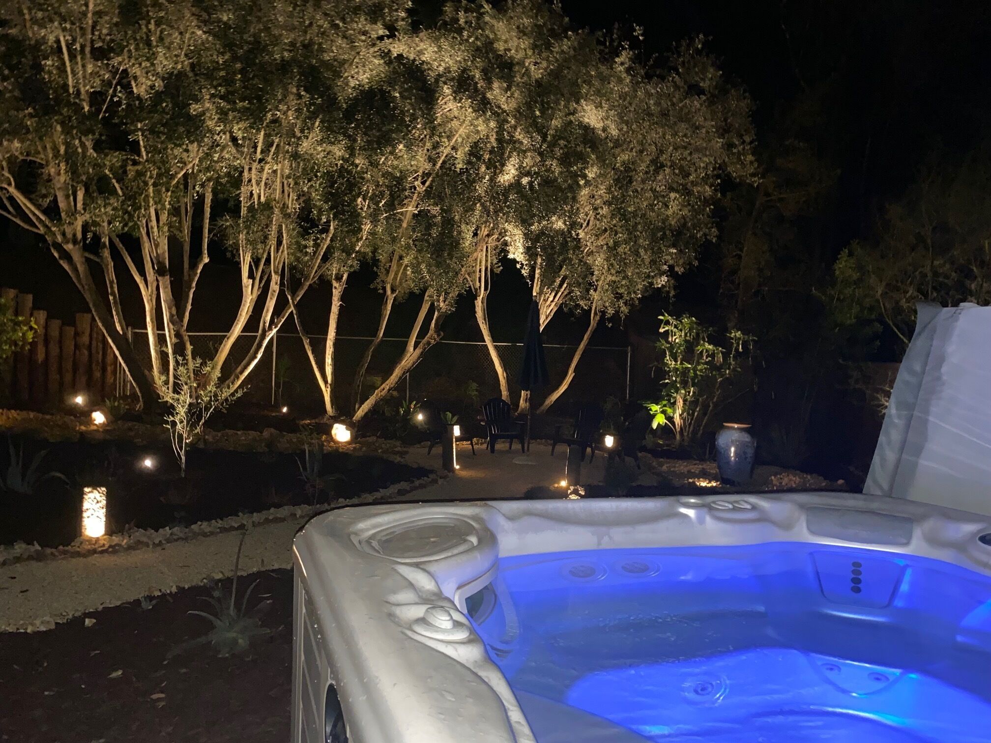 Un bain à remous dans un jardin, la nuit, avec des arbres et des lumières.