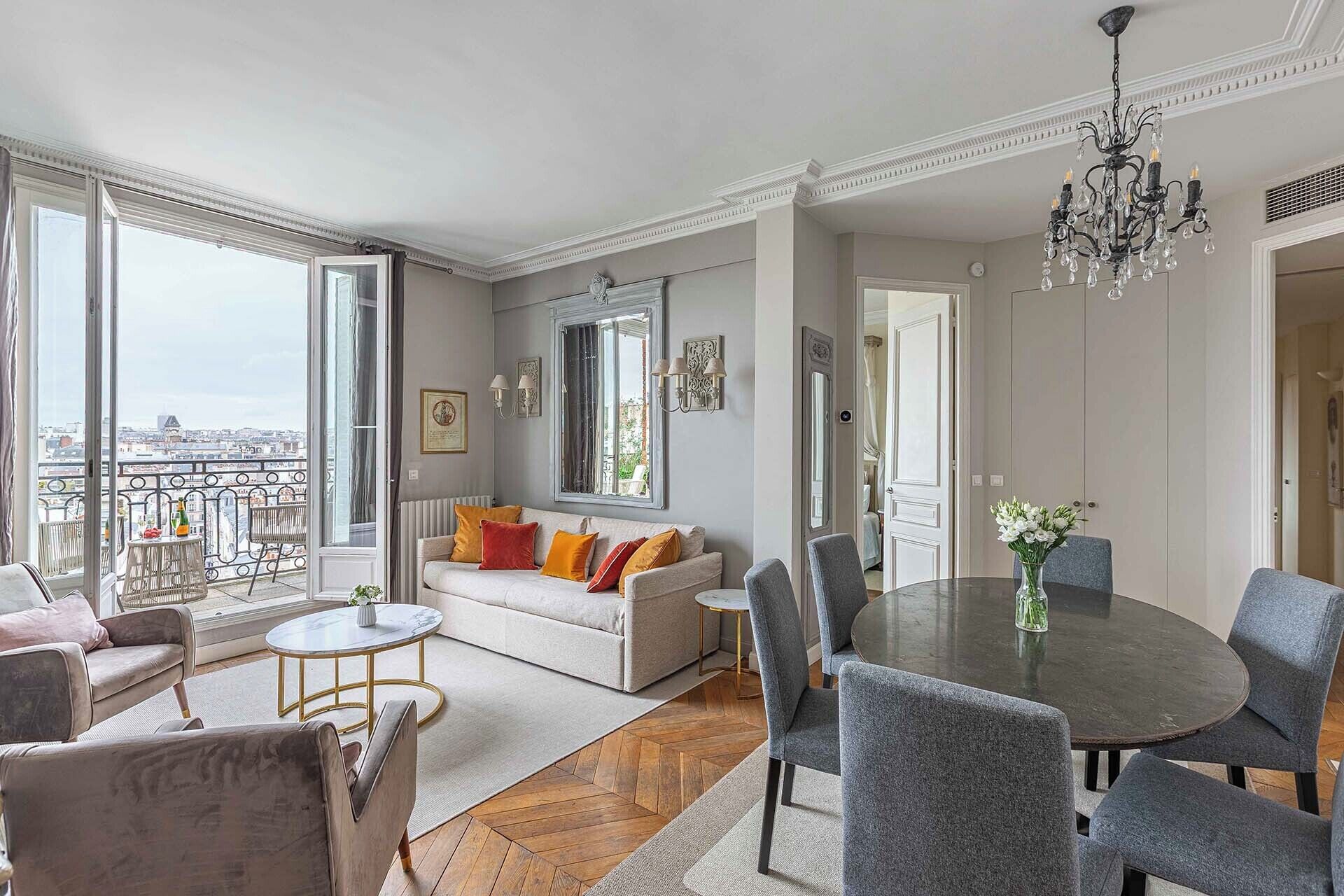 A spacious living area with a sofa, chairs, a dining table, and a balcony with a city view.