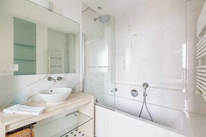 A modern bathroom with a bathtub, a glass-enclosed shower, a large mirror, and a white sink. - Stunning & Bright, Sleeps 6, w/Big Balcony and Amazing Paris Views (Paris)