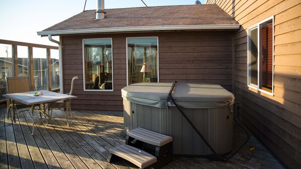 Una terraza de madera con un jacuzzi, una mesa y sillas.