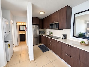 A modern kitchen with dark wooden cabinets, a stainless steel refrigerator, a microwave, and a sink.