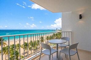 A balcony with a view of a beach and ocean, featuring a table and chairs. - Beachfront *King *Pool *Washer/D *Walk 2 Dining (Carolina)