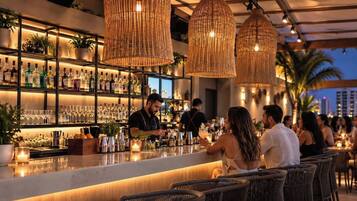 Eine Bar mit Barkeeper, Flaschenregalen und Korbstühlen.