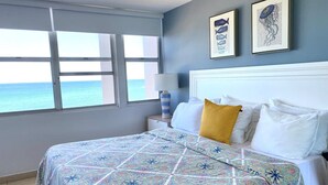 Een slaapkamer met een bed, een nachtkastje, een lamp en uitzicht op de oceaan.