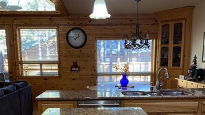 A kitchen with granite countertops, wooden cabinets, a built-in dishwasher, and a window with blinds.