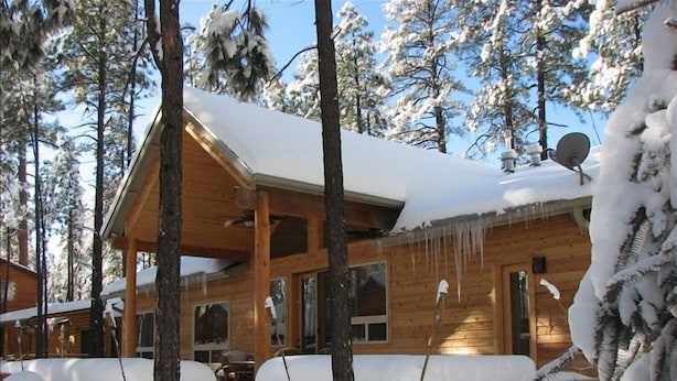 A wooden cabin with a covered deck and snow-covered surroundings.