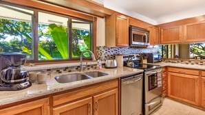 Una cocina moderna con armarios de madera, electrodomésticos de acero inoxidable, un ventanal con vistas a zonas verdes y un salpicadero de azulejos.