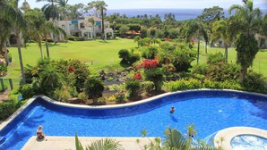 Una piscina de borde curvo, rodeada de abundante vegetación y palmeras.