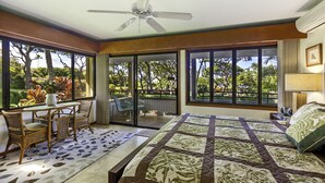 Un dormitorio con una cama grande, un comedor con sillas, un ventilador de techo y vistas al exterior.