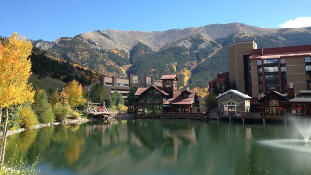 A lakeside hotel with a view of mountains, a dock, and a fountain.