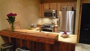 A kitchen with wooden cabinets, a stainless steel refrigerator, a microwave, and a wooden bar with stools.