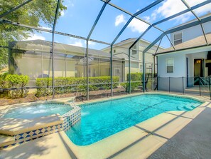 A swimming pool with a hot tub, surrounded by a covered patio area with a view of houses in the background.