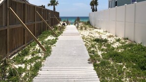 Une promenade en bois menant à la plage, bordée de clôtures en bois et d’immeubles dotés de balcons.