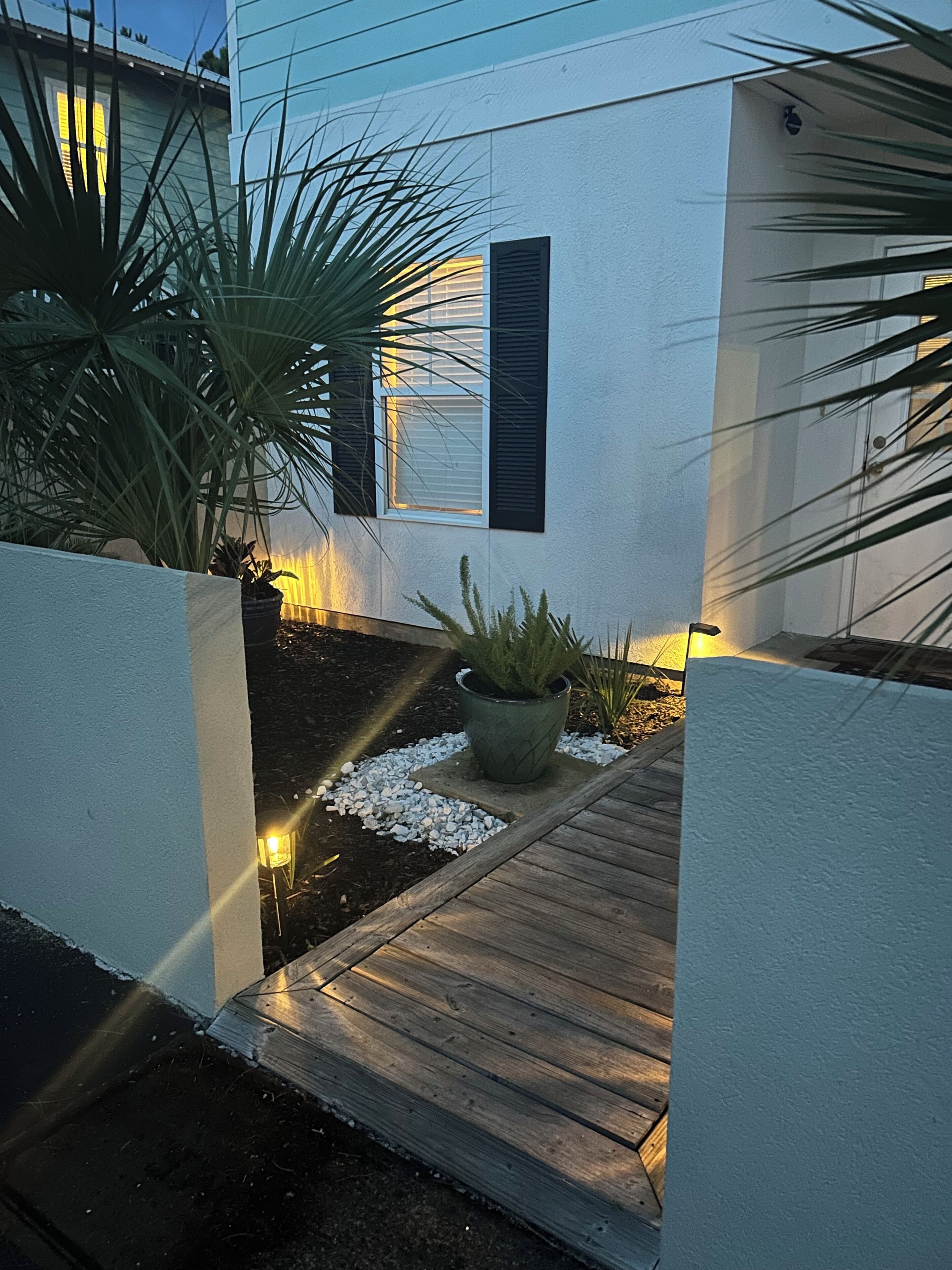 A modern house with a white exterior, a wooden deck, and a potted plant in the foreground.