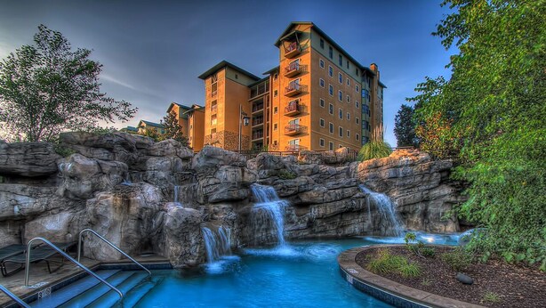 Un albergo con piscina, una cascata e un edificio con numerosi balconi.