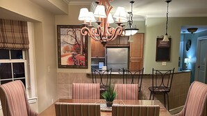 Un'area da pranzo con tavolo in legno e sedie imbottite a righe, un lampadario e un quadro appeso al muro.