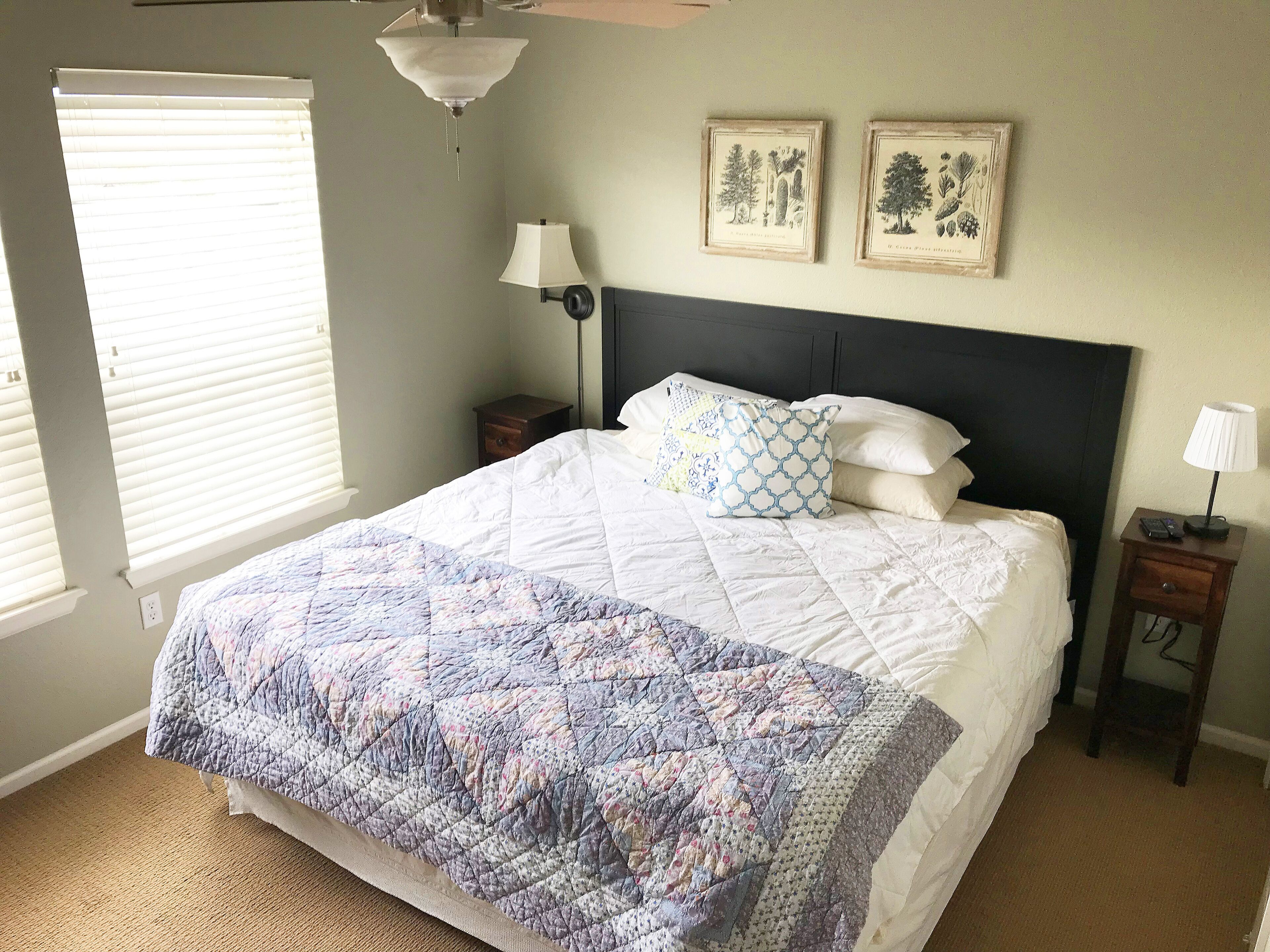 A bedroom with a large bed, a nightstand, a lamp, and two wall-mounted pictures.