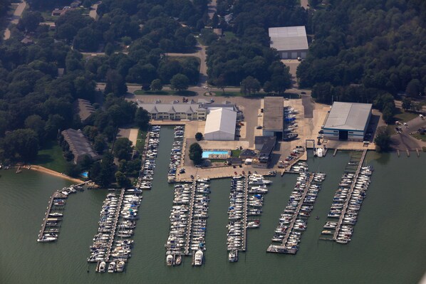 An aerial view of a marina with numerous boats docked, surrounded by trees and buildings.