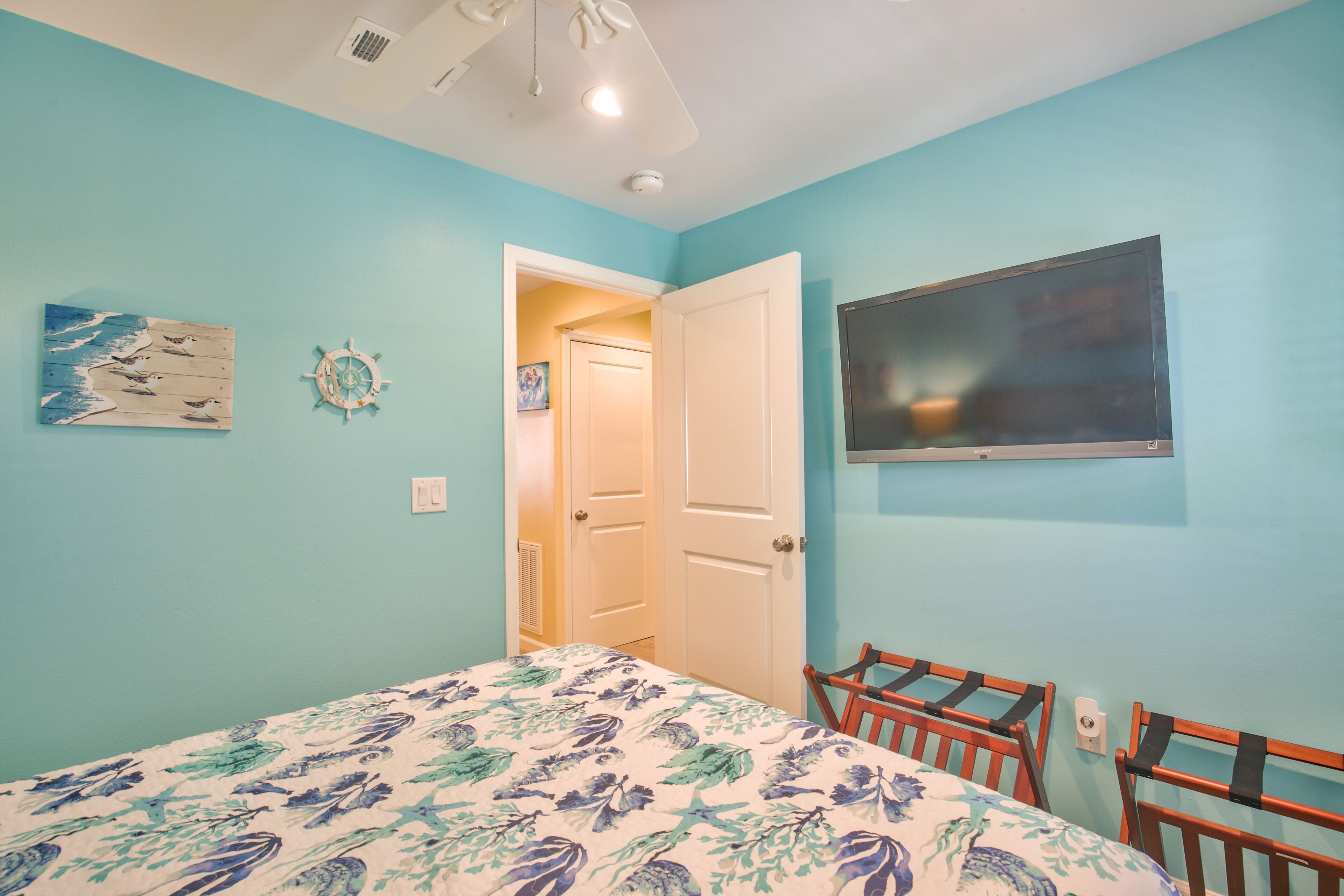 A bedroom with a bed, a TV, a door, and a ceiling fan.