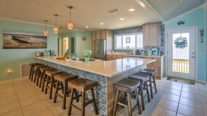 A spacious kitchen with a large island, bar stools, pendant lights, and a view to the outside. - 7 Bedroom Beach House with POOL!! Gulf Front and Bay Front (Alligator Point)