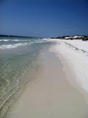 Una playa con aguas cristalinas, arena blanca y un barco a lo lejos.