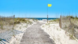 A wooden pathway leading to a beach with a yellow flag.