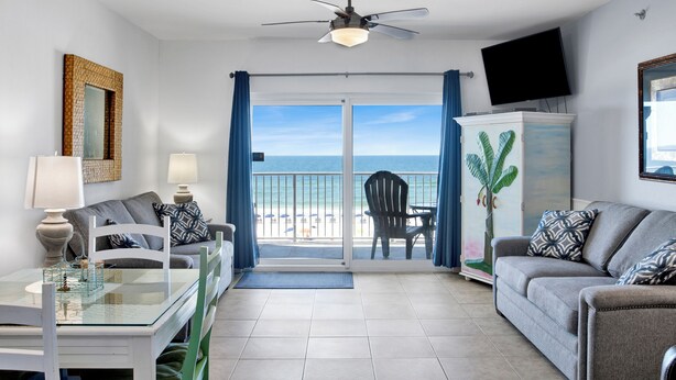 A room with a glass table, two sofas, a TV, and a view of the beach.