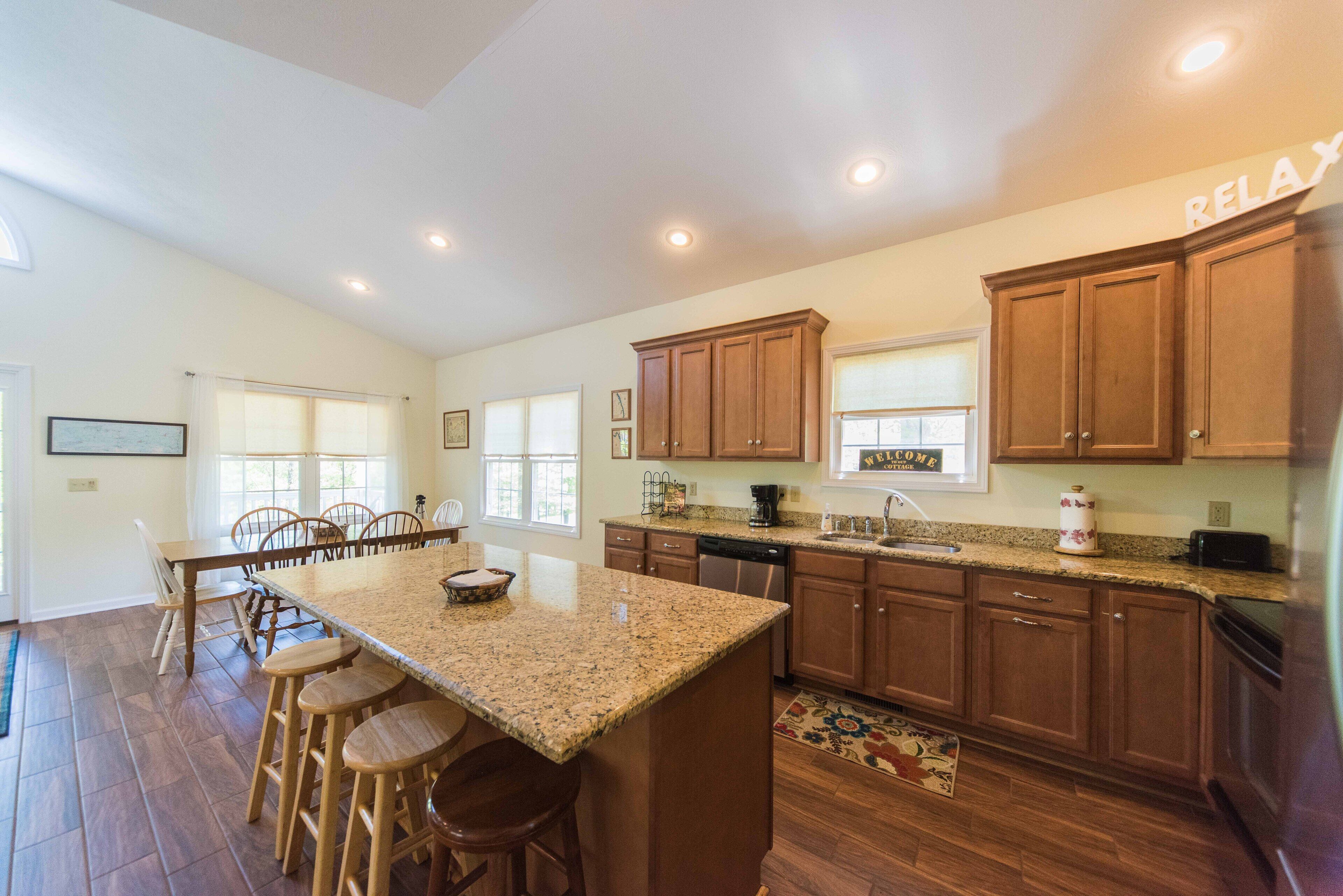 A spacious kitchen with wooden cabinets, a granite countertop, and a central island with bar stools.