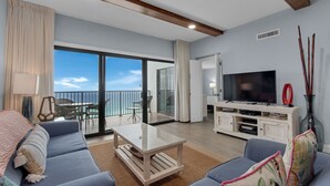 Un salon moderne avec un canapé, une table basse en verre, un téléviseur et un balcon offrant une vue sur la mer.