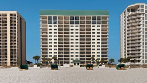 Un hôtel situé en bord de mer, avec plusieurs étages, des balcons et une plage de sable devant.