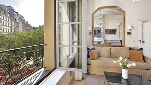 Un balcone con vista sugli edifici parigini, un divano con cuscini, un tavolino da caffè in vetro e un grande specchio che riflette un lampadario e un quadro.