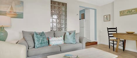A living room with a grey sofa, a coffee table, and a dining area with a wooden table and chairs.