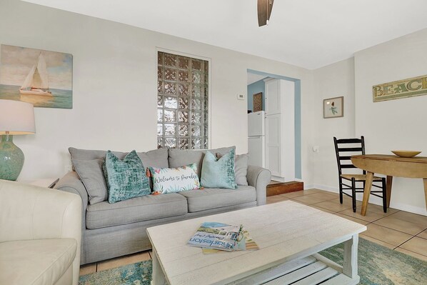 A living room with a grey sofa, a coffee table, and a dining area with a wooden table and chairs.